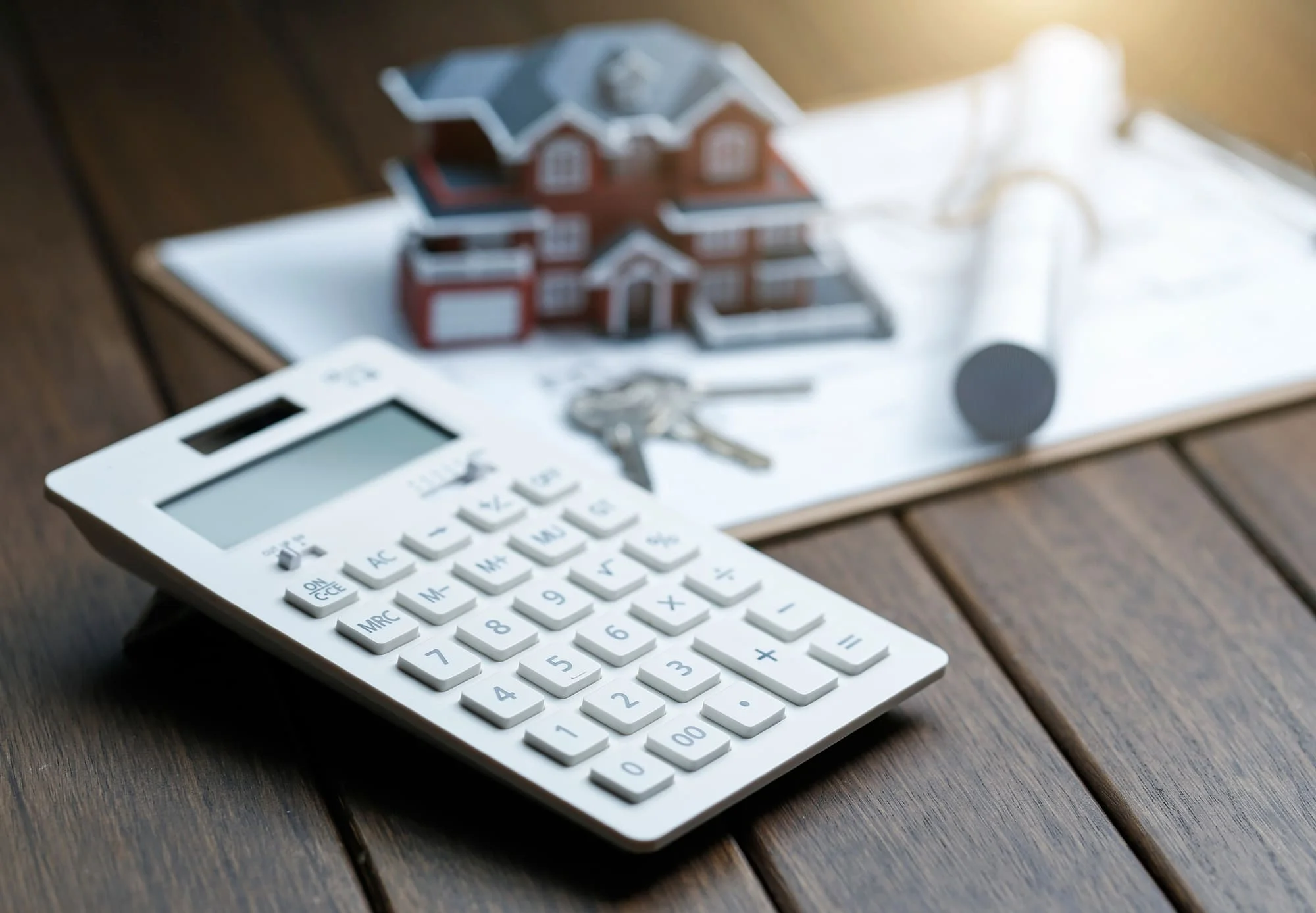 Calculator, small house model, keys and a blueprint on a wooden table