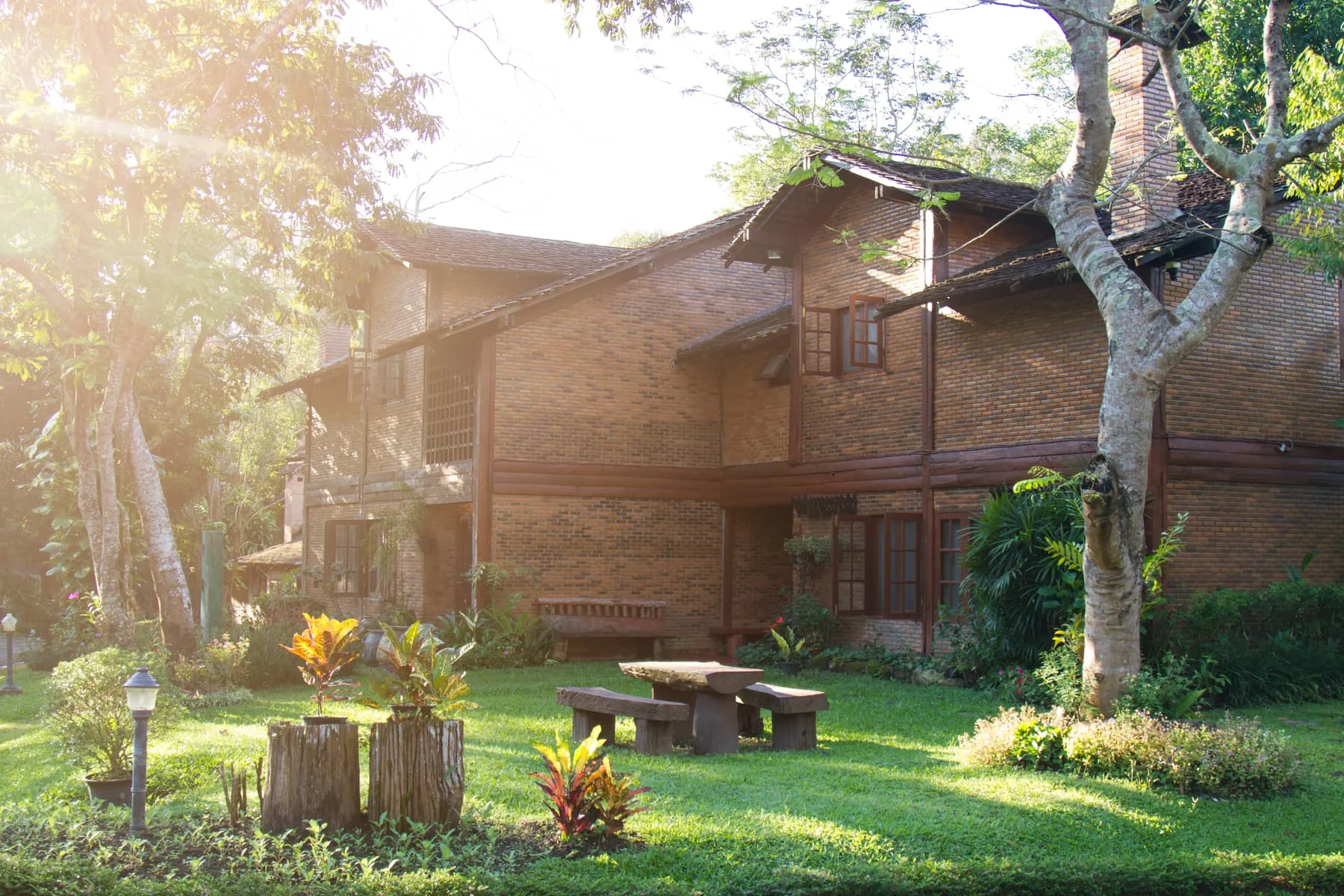 Brick house with a sunlit lawn, mature trees and a garden seating area