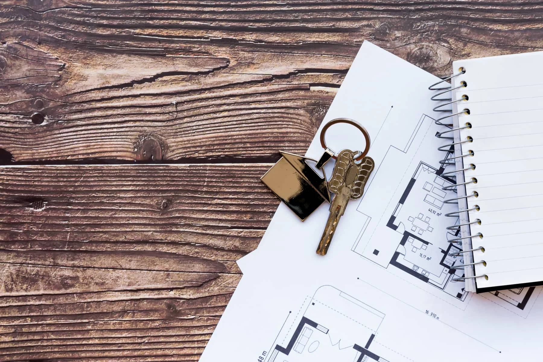 House keys resting on a blueprint and a spiral notebook on a wooden desk