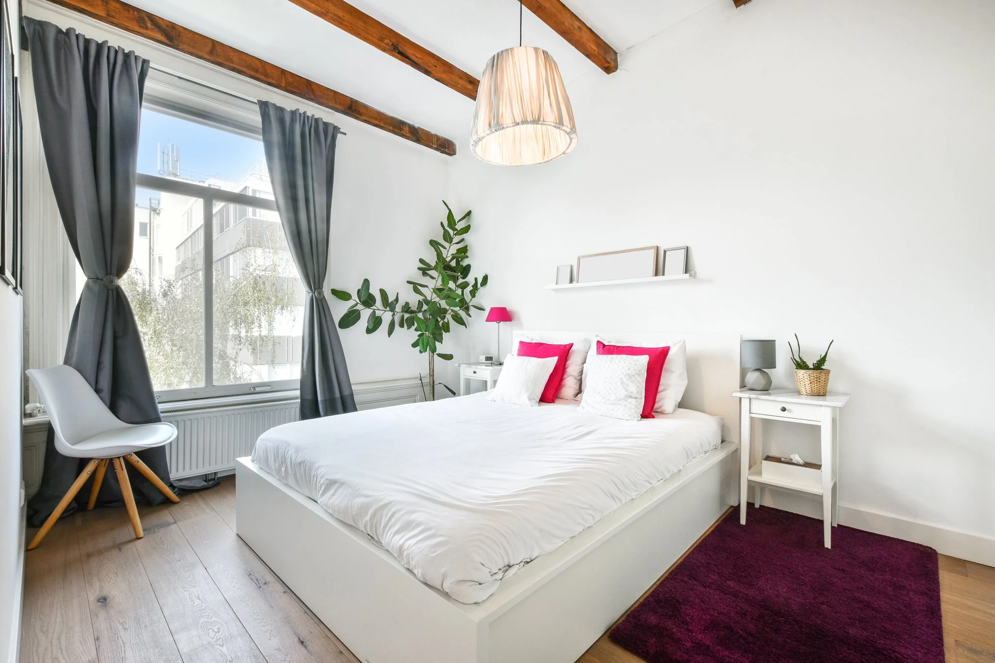 Bright bedroom with a white bed, wooden ceiling beams and a large window