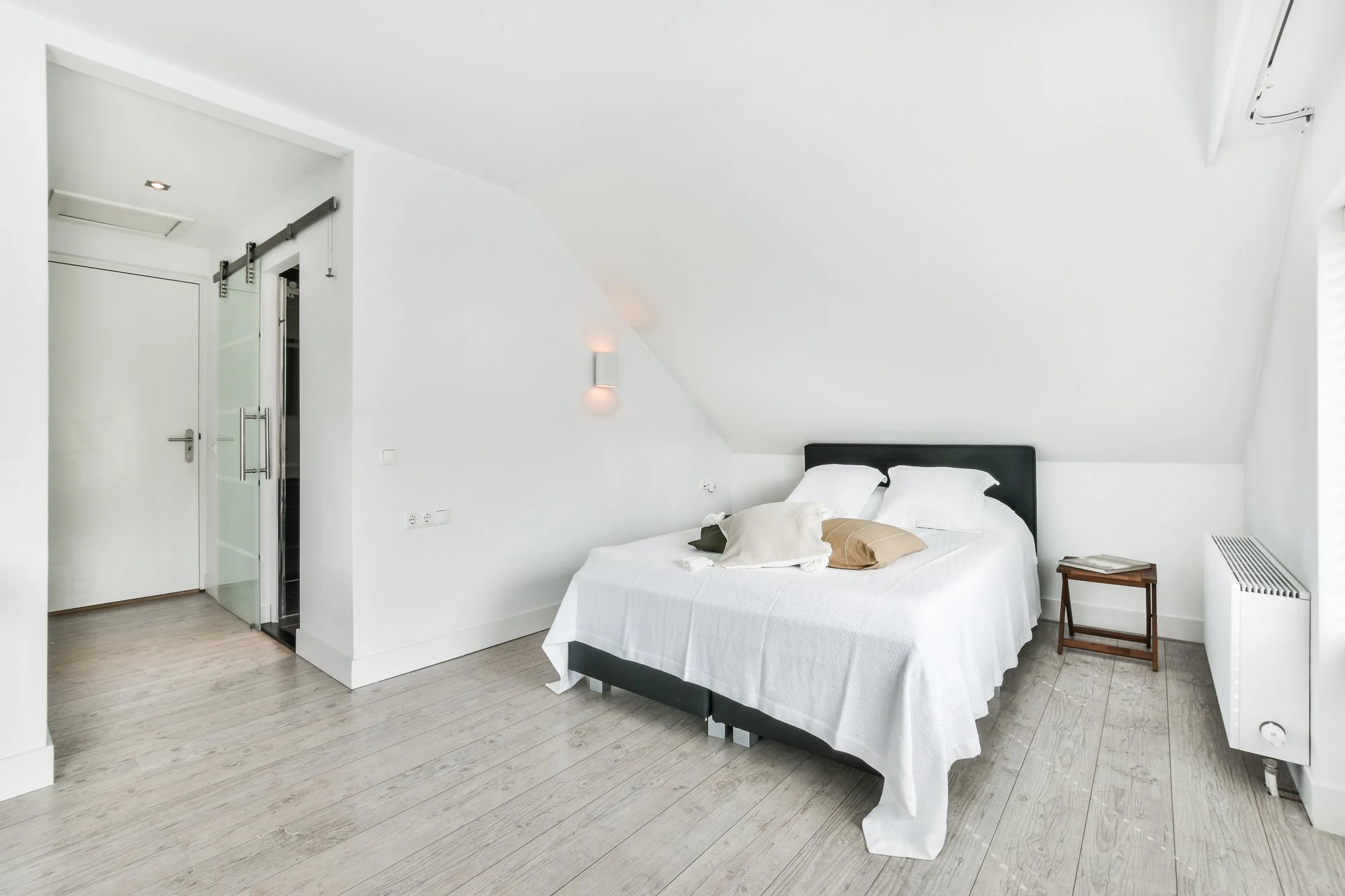 White attic bedroom with a double bed, gray floor and a sliding glass door