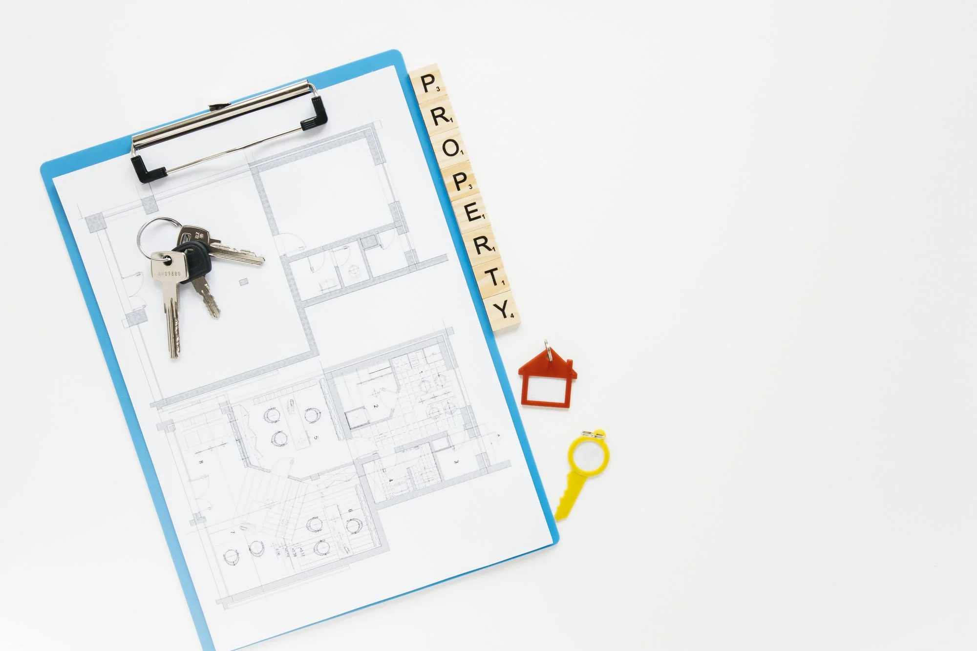 Clipboard with a floor plan, house keys and lettered tiles spelling the word property on a white surface