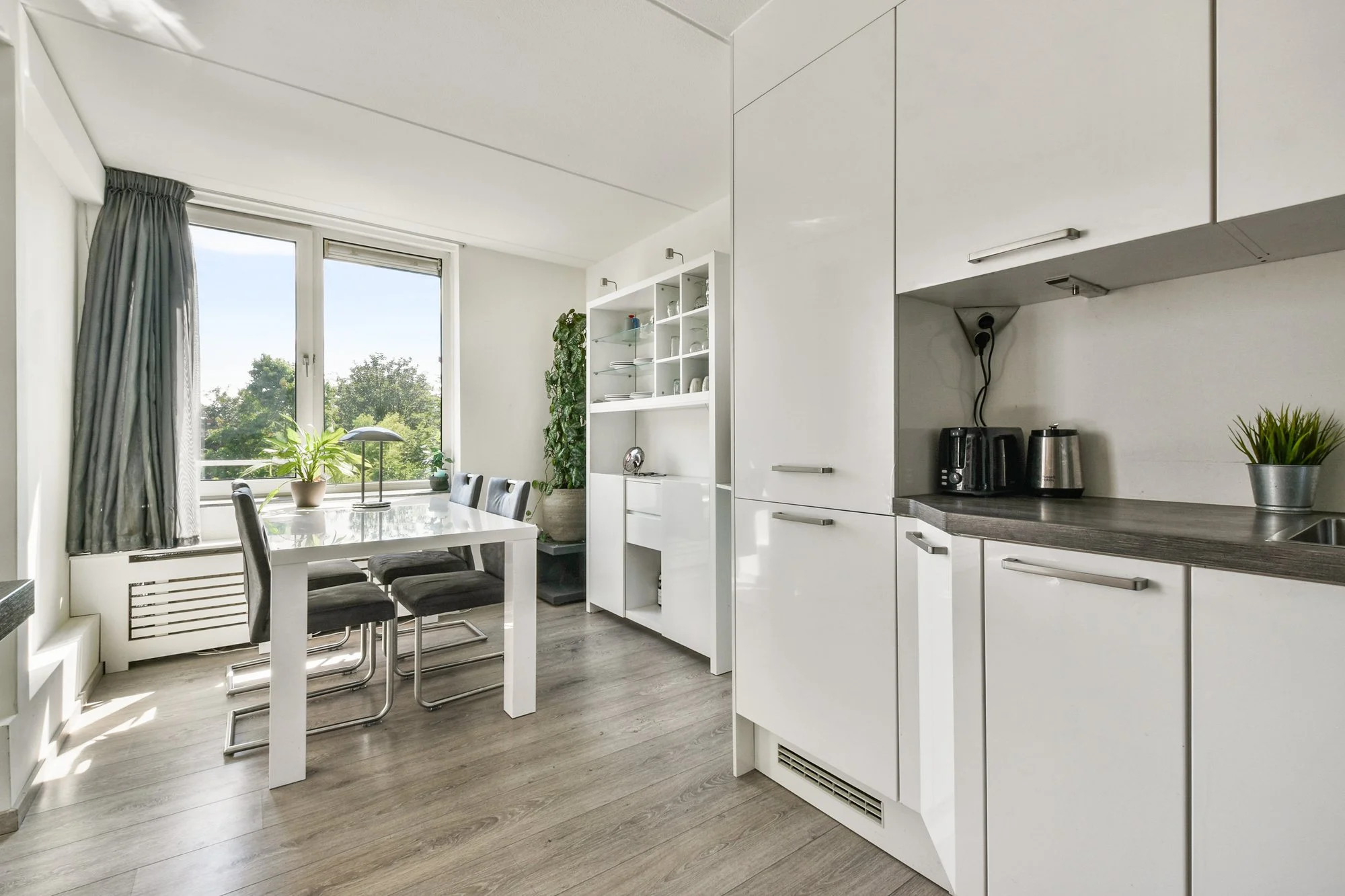 Compact white kitchen with a dining table by a window and a gray floor