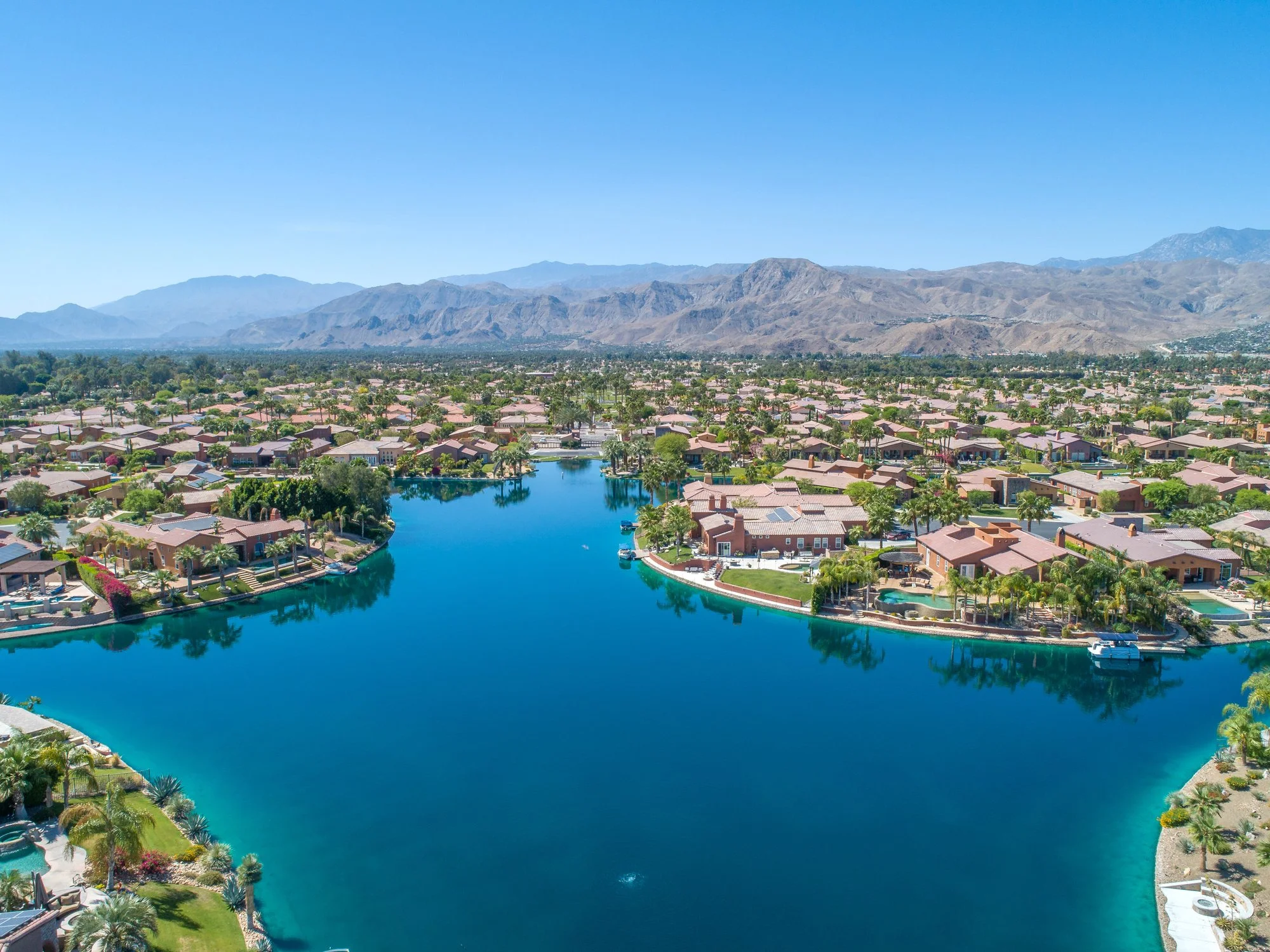 Aerial view of a lakeside residential community with mountains in the distance under a clear sky