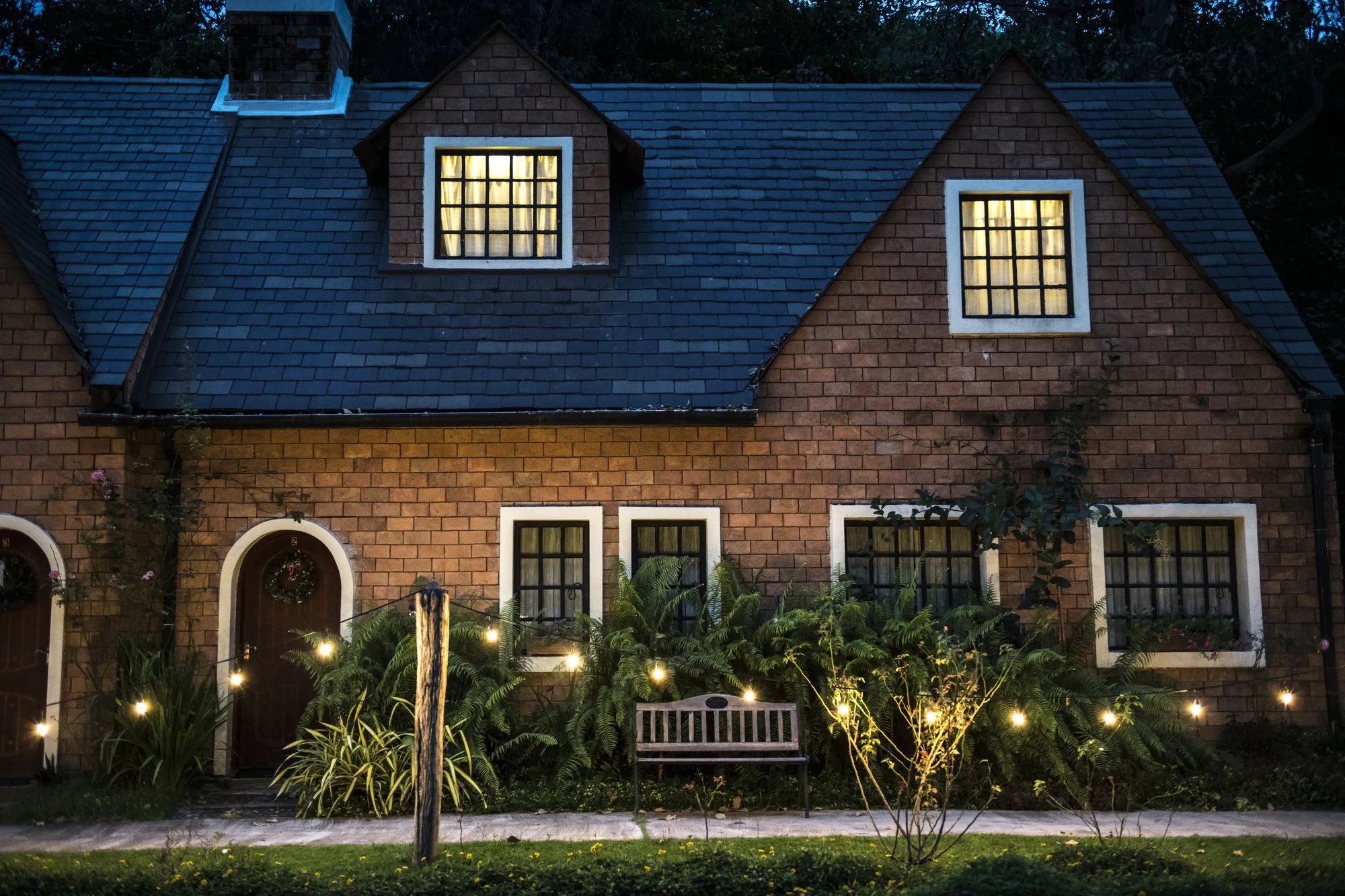 Brick house with lit windows and a garden path at dusk