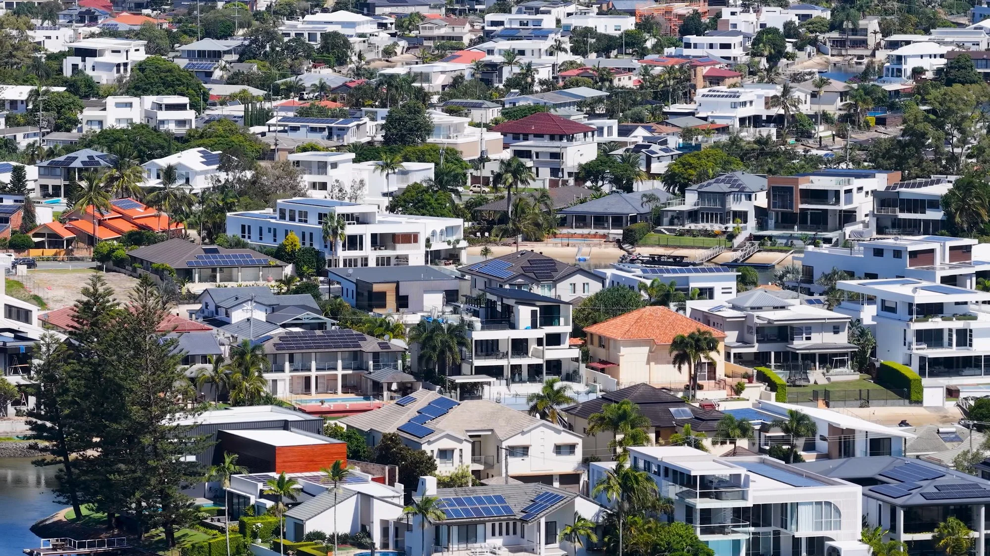 Aerial view of a hillside neighborhood of white and tile-roofed homes beside a waterway