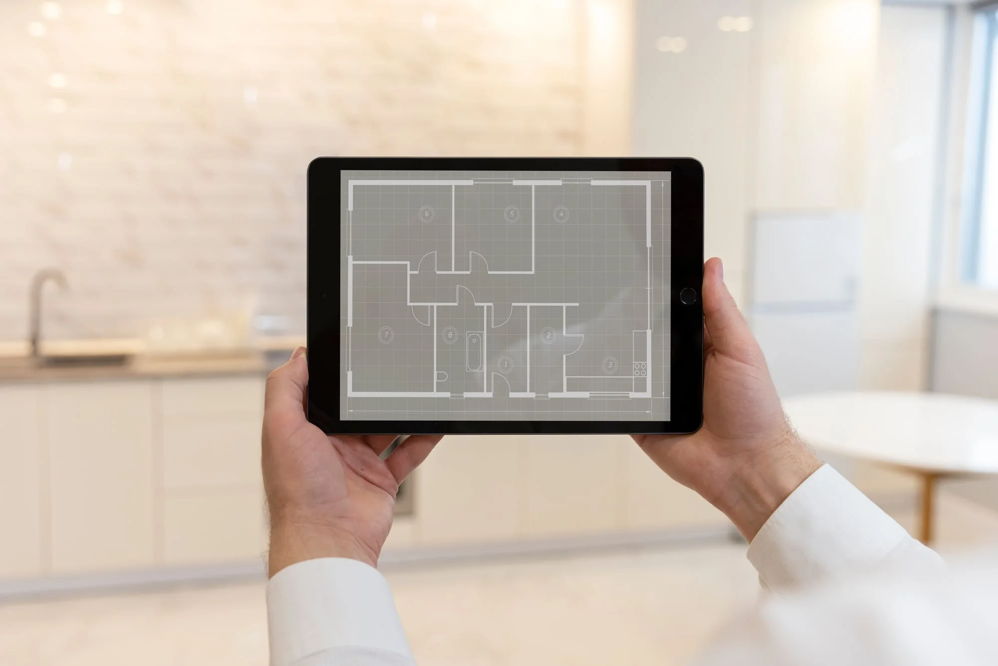 Two hands holding a tablet that shows a house floor plan